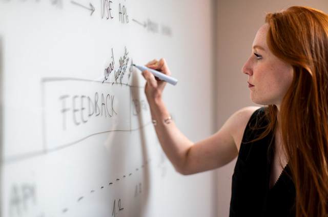 Frau notiert Projektfortschritte am Whiteboard – Symbol für Projektmanagement national und international und erfolgreiche Projektumsetzung