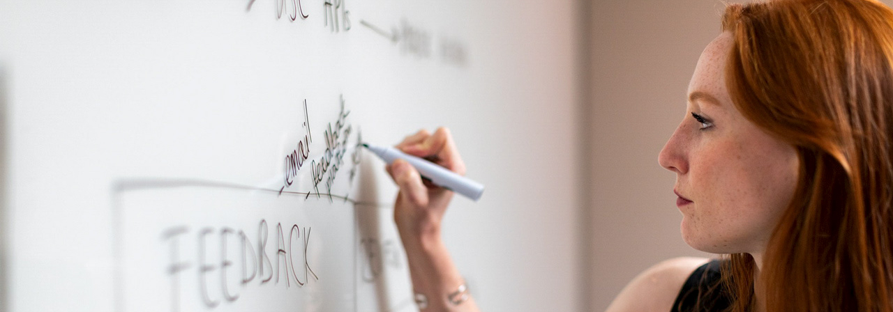 Projektmanagement national und international. Frau beschreibt auf einem Whiteboard den Projektfortschritt.